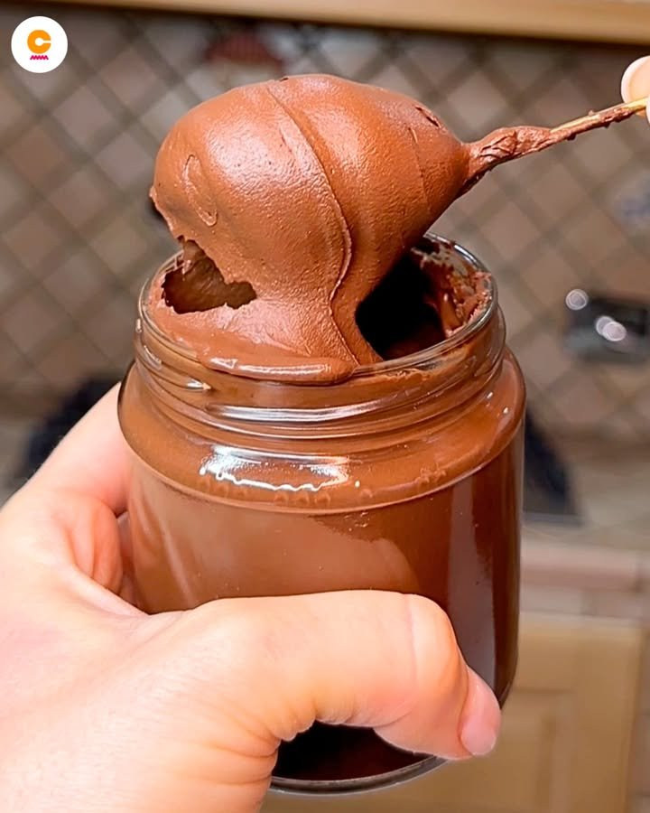 Crema marrone al cioccolato sollevata da un cucchiaio sopra un vasetto